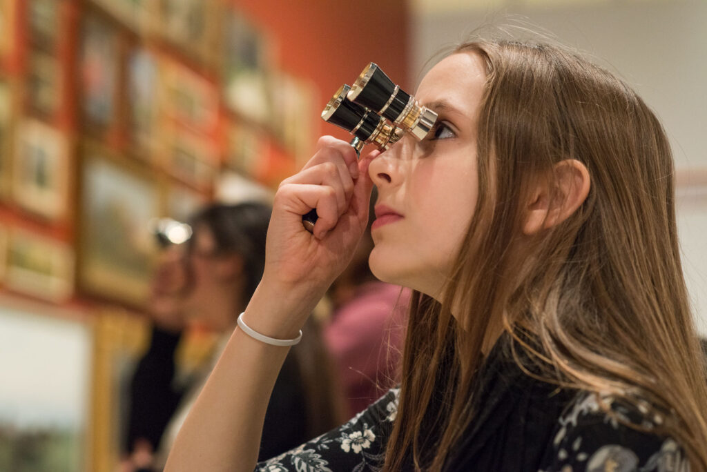 Young girls using special binoculars to look at framed art hung on a wall
